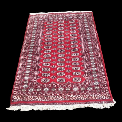 597 - A VINTAGE WOOLLEN BOKHARA RUG
With numerous elephant guls contained within running borders on a red ... 