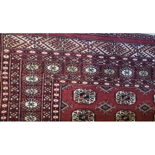 597 - A VINTAGE WOOLLEN BOKHARA RUG
With numerous elephant guls contained within running borders on a red ... 