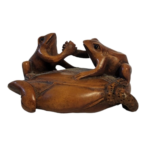 276 - A 20TH CENTURY JAPANESE CARVED WOODEN NETSUKE
Two frogs shaking hands on a lily pad, signed to base.... 