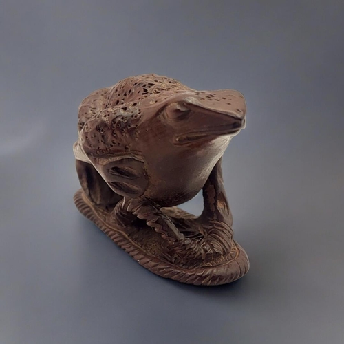 294 - A JAPANESE WOODEN TOAD NETSUKE
Sat on a sandal with maker’s mark to base. 
(5.5cm x 3cm x 4cm)

Cond... 