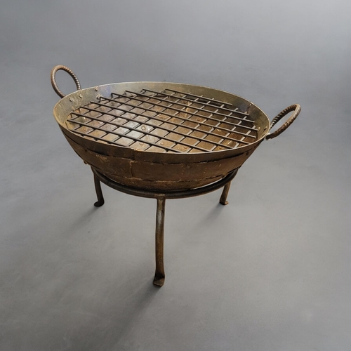 295 - A CAST IRON FIRE PIT
With ring handles and riveted body, inserted griddle and detachable tripod stan... 