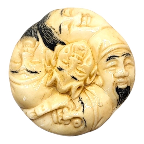 308 - A JAPANESE BONE NETSUKE
Circular form, with carved stylised faces to body. 
(4cm x 1.5cm)

Condition... 