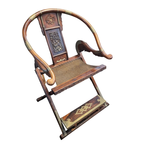 495 - A CHINESE SOLID HUANGHUALI FOLDING HORSE SHOE CHAIR, with brass mounts and carved and pierced panels... 