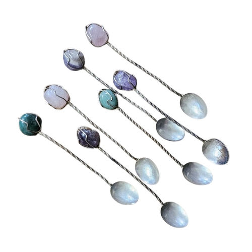 141 - A SET OF WHITE METAL AND GEMSET APERITIF SPOONS 
A set of seven each features a twisted stem topped ... 