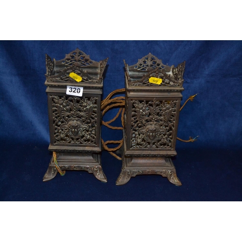 320 - PAIR OF ORNATE PIERCED BRONZE CANDLE HOLDERS WITH MASK DECORATION ON SCROLL FEET (CONVERTED TO ELECT... 