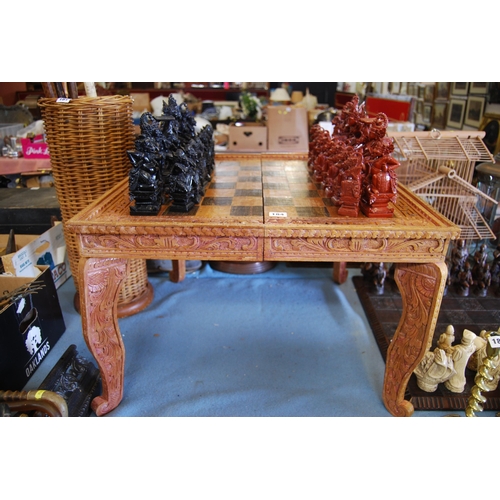184 - RICHLY CARVED INDONESIAN CHESS SET ON CARVED TABLE WITH CHESS BOARD TOP AND DETACHABLE LEGS
