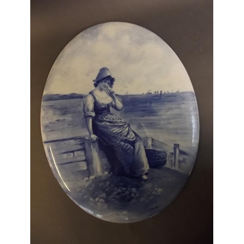 31 - A Doulton Burslem blue and white oval plaque depicting a Dutch girl sitting on a breakwater, signed ... 