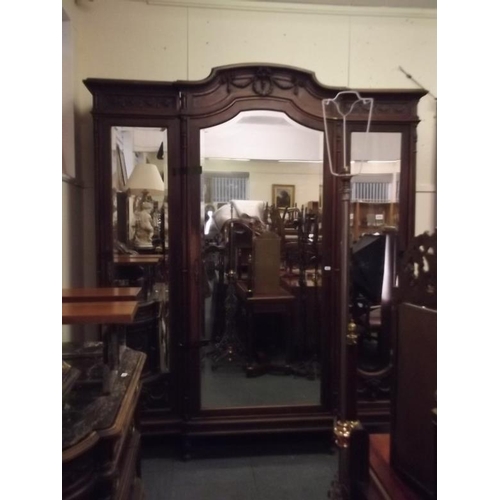 915 - An imposing Italian walnut breakfront armoire with bevelled mirror doors and carved classical decora... 