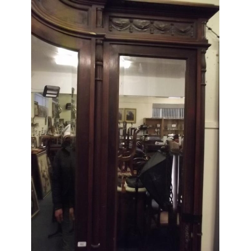 915 - An imposing Italian walnut breakfront armoire with bevelled mirror doors and carved classical decora... 