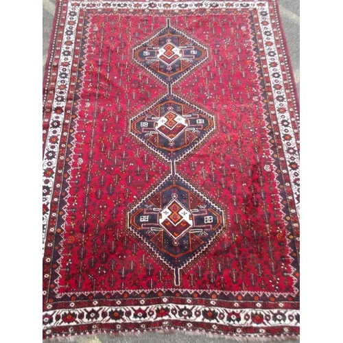 835 - A Persian wool carpet with central lozenge design on a red field with ivory borders, 86