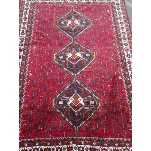 835 - A Persian wool carpet with central lozenge design on a red field with ivory borders, 86