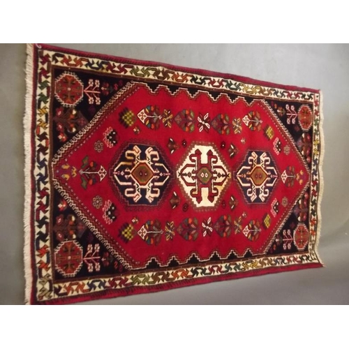 854 - A Persian wool rug with geometric design on a bright red field, 63