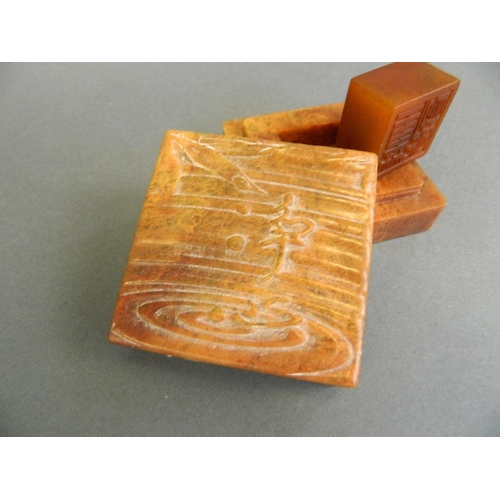 91 - A Chinese mottled orange soapstone box opening to reveal an amber soapstone seal, the lid with carve... 