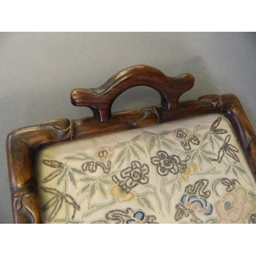 355 - An Oriental hardwood tray with a glazed silk embroidered panel, the frame and handles carved as bamb... 