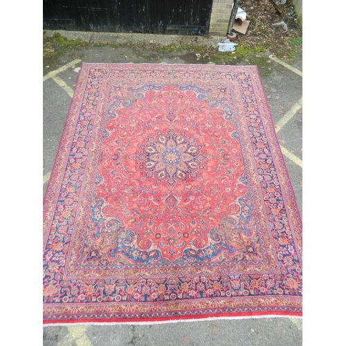 863 - A large antique red ground Persian Kashan carpet with medallion design on a blue field within a flor... 