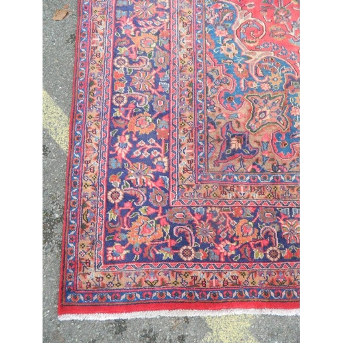 863 - A large antique red ground Persian Kashan carpet with medallion design on a blue field within a flor... 