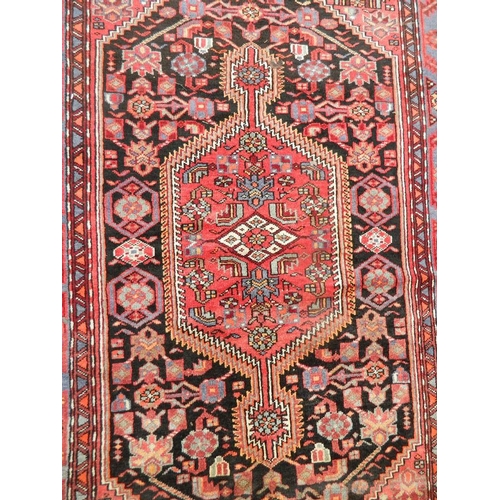 869 - A hand woven Persian Hamadan Luri carpet with all over design on a red field, 55