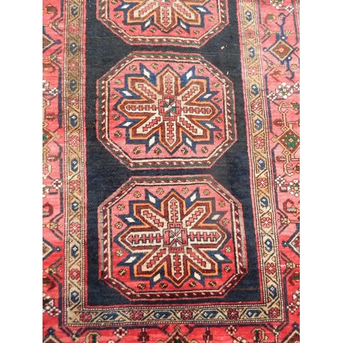 879 - A Persian Hamadan Luri carpet with bespoke medallion design on a red and ebony field, 52