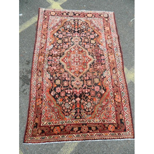 889 - A hand woven Persian village carpet with floral medallion design on an ebony ground, 48