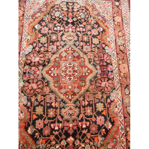 889 - A hand woven Persian village carpet with floral medallion design on an ebony ground, 48