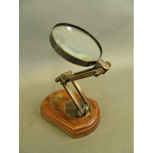 106 - A magnifying glass in an adjustable frame, mounted on a wooden base, bears label 'Watts & Sons Ltd.,... 