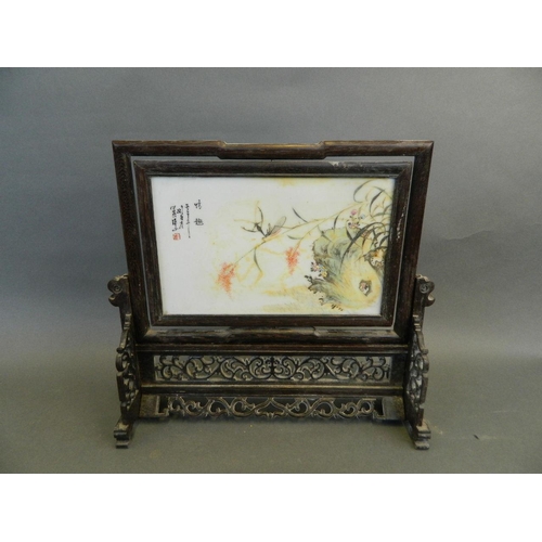 58 - A Chinese carved and pierced hardwood revolving table screen containing a porcelain plaque decorated... 