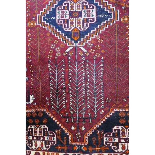 869 - A Persian wool carpet with central medallion design and stylised trees, on a red field with cream bo... 