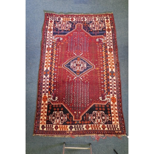 869 - A Persian wool carpet with central medallion design and stylised trees, on a red field with cream bo... 