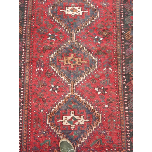 877 - A red ground Persian village rug decorated with three central medallions, A/F slight tears to corner... 