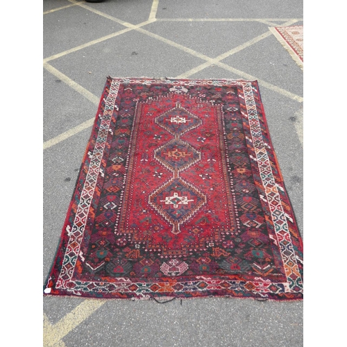 877 - A red ground Persian village rug decorated with three central medallions, A/F slight tears to corner... 