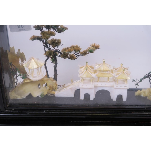 39 - An Oriental mother of pearl and abalone model of a lakeside temple, with trees and cranes, in a glas... 