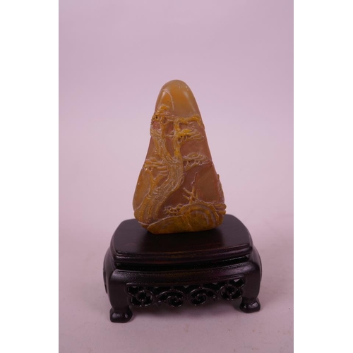 59 - A Chinese carved amber soapstone ornament decorated with figures in a landscape scene, mounted on a ... 