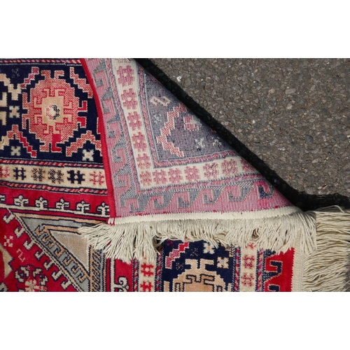 1219 - A red ground Persian style rug with a triple medallion decoration and blue border, 120