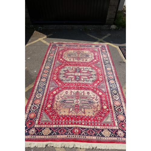 1219 - A red ground Persian style rug with a triple medallion decoration and blue border, 120