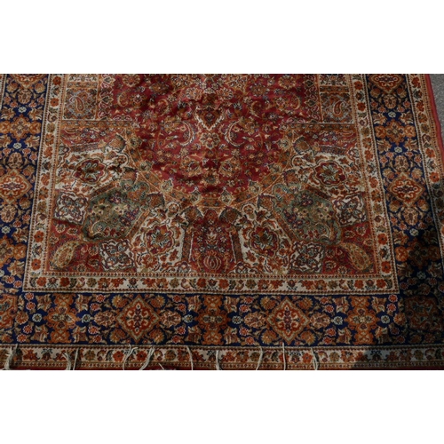 1221 - An Oriental carpet with blue borders and floral designs on a red field, 60