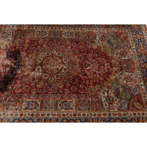 1221 - An Oriental carpet with blue borders and floral designs on a red field, 60