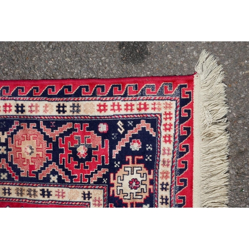 1219 - A red ground Persian style rug with a triple medallion decoration and blue border, 120