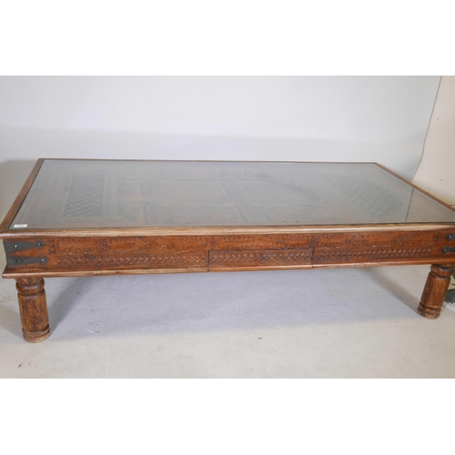 1204 - An Indian carved hardwood table with glass top and two frieze drawers, raised on turned supports