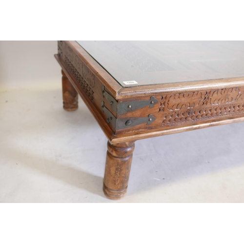 1204 - An Indian carved hardwood table with glass top and two frieze drawers, raised on turned supports