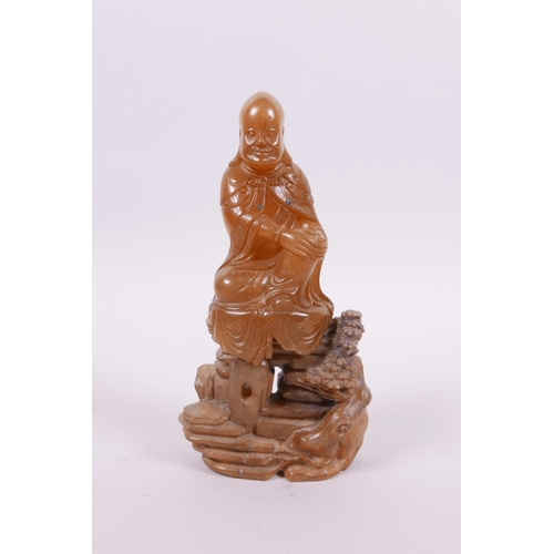 71 - A Chinese natural amber soapstone carving of Shao Lao seated on a rocky outcrop, 5½