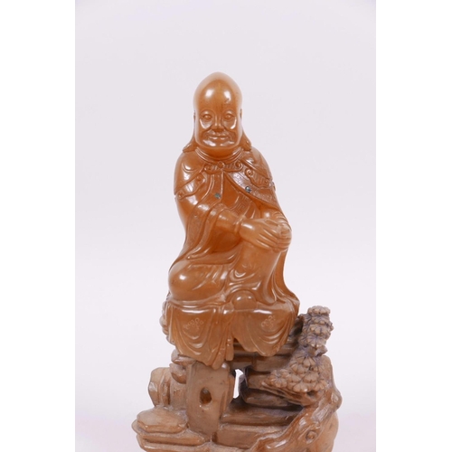 71 - A Chinese natural amber soapstone carving of Shao Lao seated on a rocky outcrop, 5½