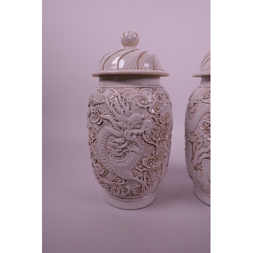 44 - A pair of Chinese white ground pottery jar and covers with raised moulded dragon decoration, impress... 