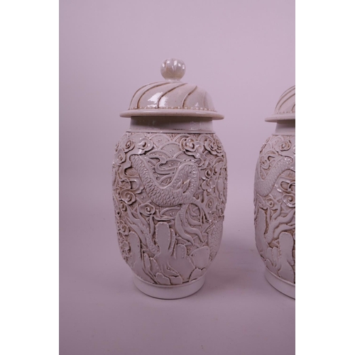 44 - A pair of Chinese white ground pottery jar and covers with raised moulded dragon decoration, impress... 