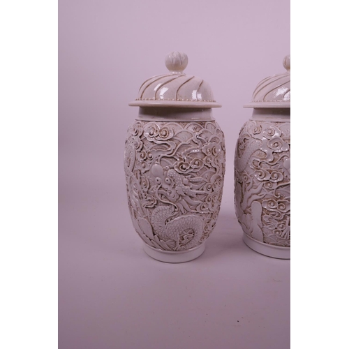 44 - A pair of Chinese white ground pottery jar and covers with raised moulded dragon decoration, impress... 