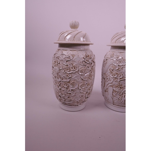 44 - A pair of Chinese white ground pottery jar and covers with raised moulded dragon decoration, impress... 