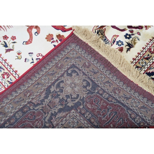 1135 - A red and ivory ground Kashmir carpet, decorated with a traditional hunting scene