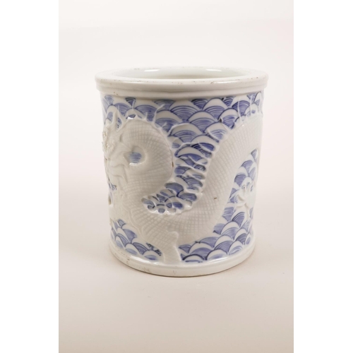 5 - A Chinese blue and white porcelain brush pot with raised decoration of a dragon catching carp, impre... 