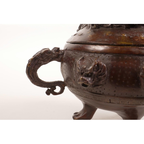 75 - A Chinese two handled bronze censer and cover on tripod paw feet, with dragon and mask decoration, 6... 