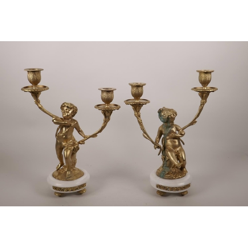 62 - A pair of ormolu two branch candlesticks in the form of putti, on marble bases,  12