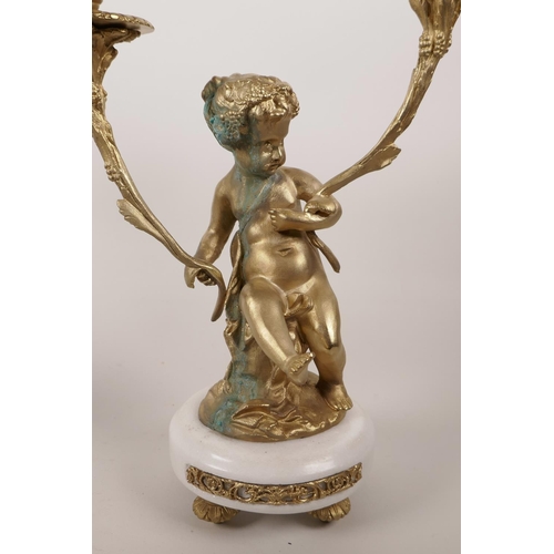 62 - A pair of ormolu two branch candlesticks in the form of putti, on marble bases,  12